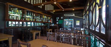 A restaurant with wooden tables and chairs, a bar area with shelves of bottles, and large windows with a view.