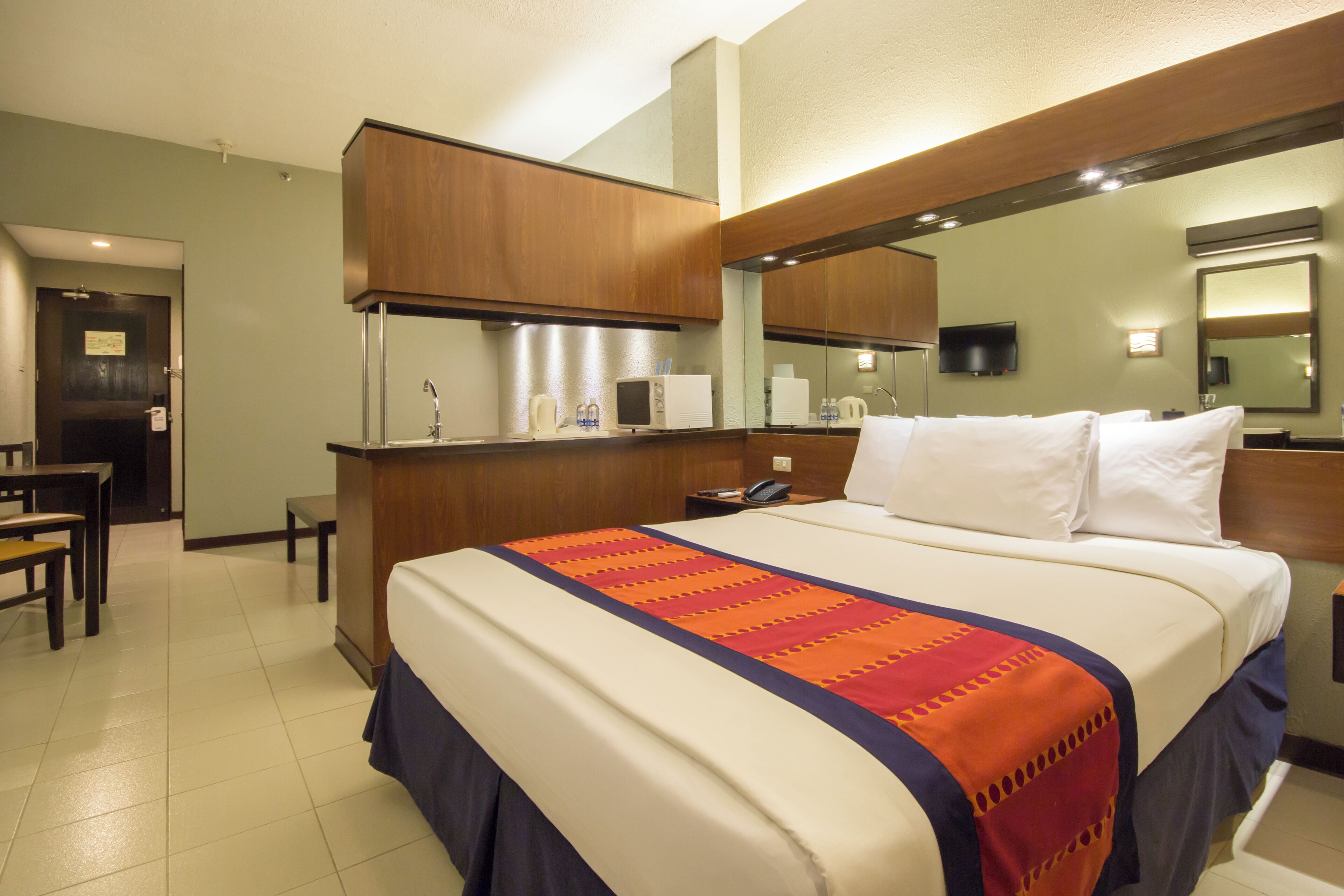 Ein Hotelzimmer mit Bett, Schreibtisch, Spiegel, Fernseher und einer Tür.