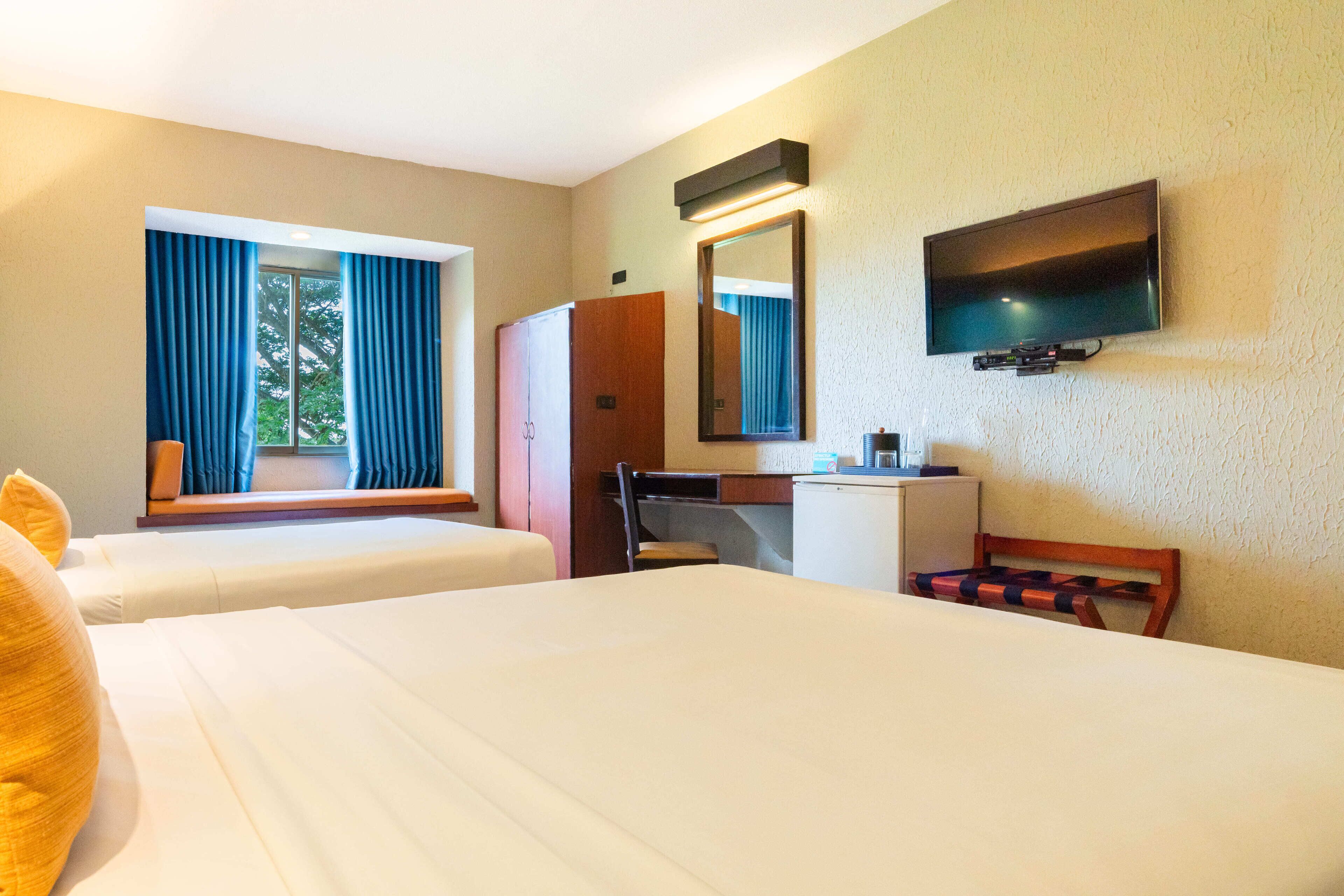 A hotel room with two beds, a desk, a chair, a television, and a window with curtains.
