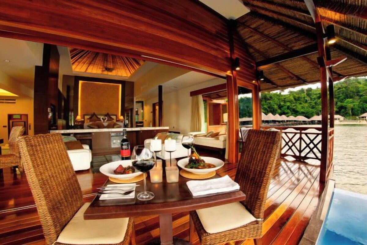 A wooden deck with a dining table set for two, surrounded by wicker chairs.