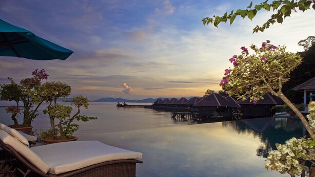 A serene poolside area with lounge chairs and potted plants, overlooking a calm body of water and overwater bungalows. - Gayana Marine Resort (Gaya Island)