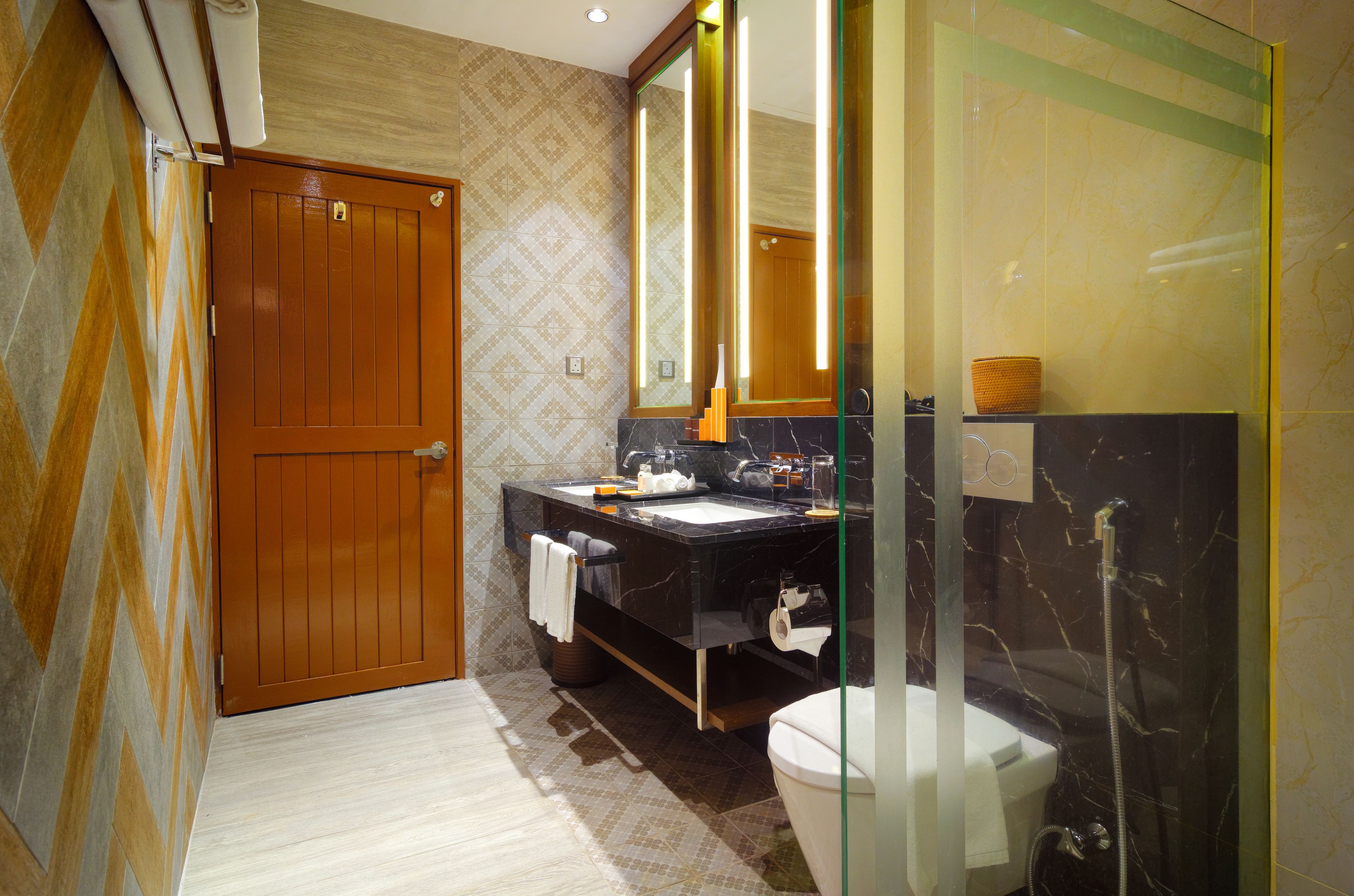 A bathroom with a wooden door, a black sink with a mirror, a white toilet, and a glass shower enclosure.