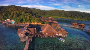 Overwater bungalows with thatched roofs, wooden walkways, and a boat docked nearby. - Gayana Marine Resort (Gaya Island)