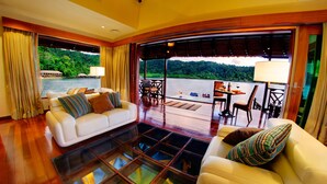 A spacious room with a large window overlooking a body of water and lush greenery. There is a white sofa with striped cushions and a dining area with a table and chairs. - Gayana Marine Resort (Gaya Island)