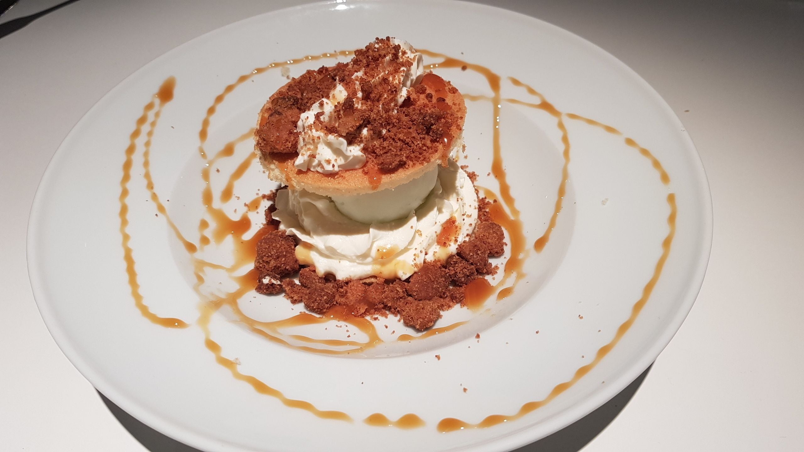 A dessert on a white plate with caramel sauce and crumbs.