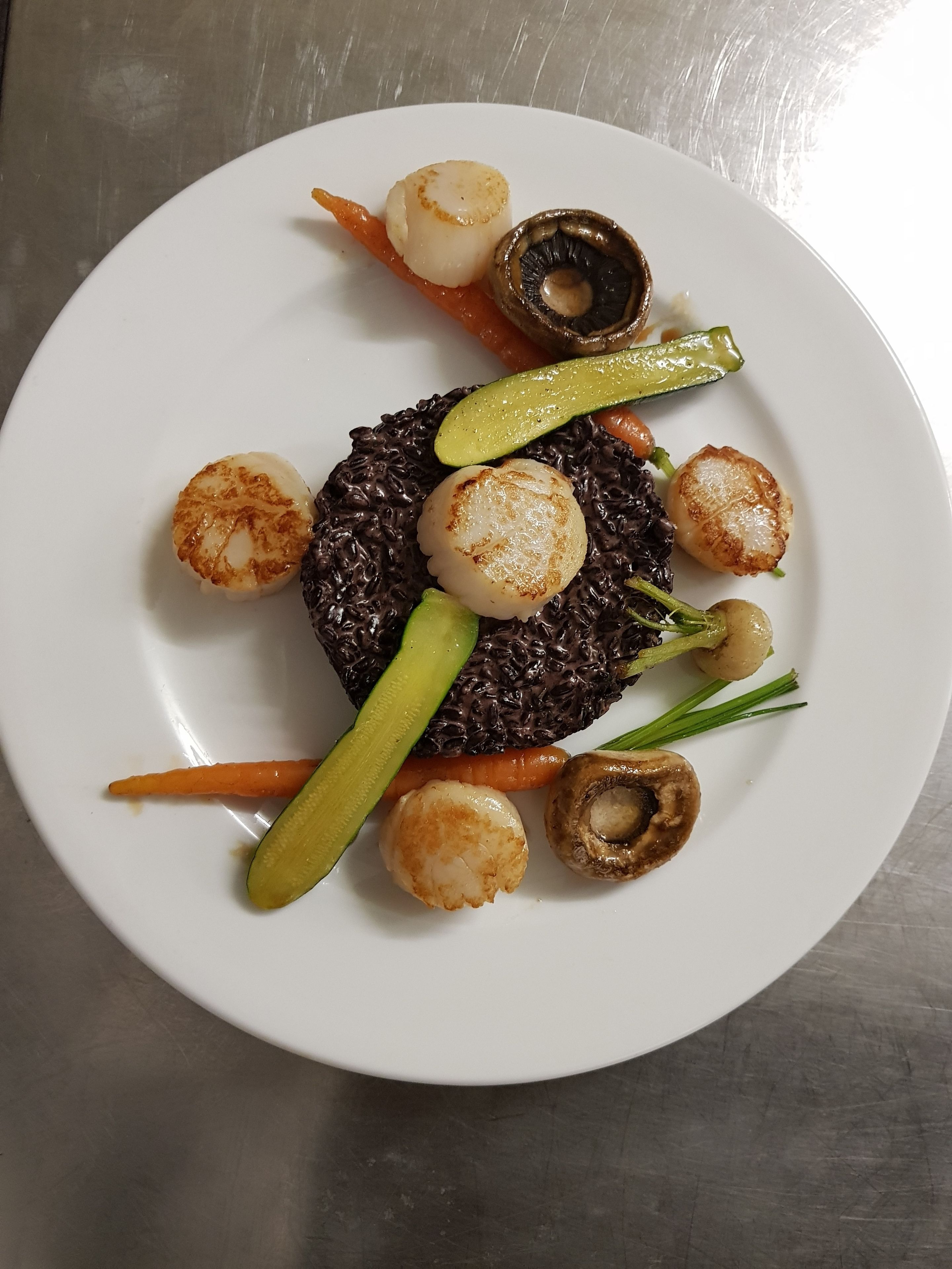 A plate with black rice, scallops, mushrooms, carrots, and pickles.