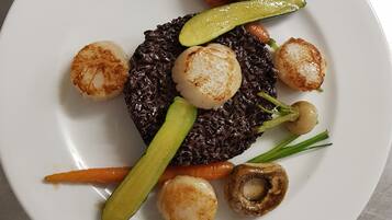 Um prato com arroz preto, vieiras, cogumelos, cenouras e picles.