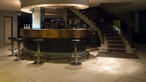 Uma área de bar com balcão circular, banquetes e uma escada ao fundo.