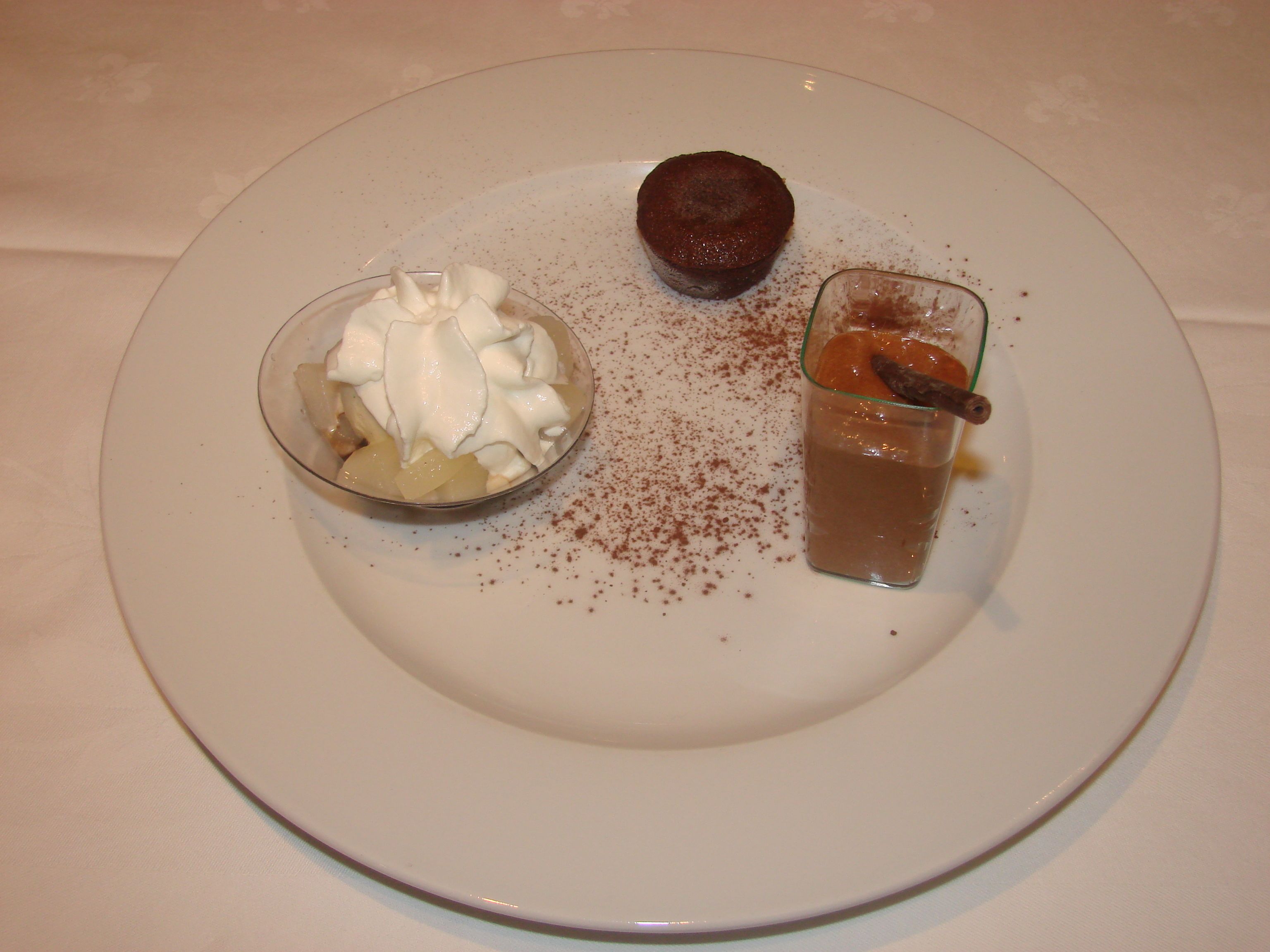 Ein Dessertteller mit einer Schüssel Schlagsahne und Früchten, ein Schokoladendessert und ein Glas Schokoladengetränk mit Zimtstange.