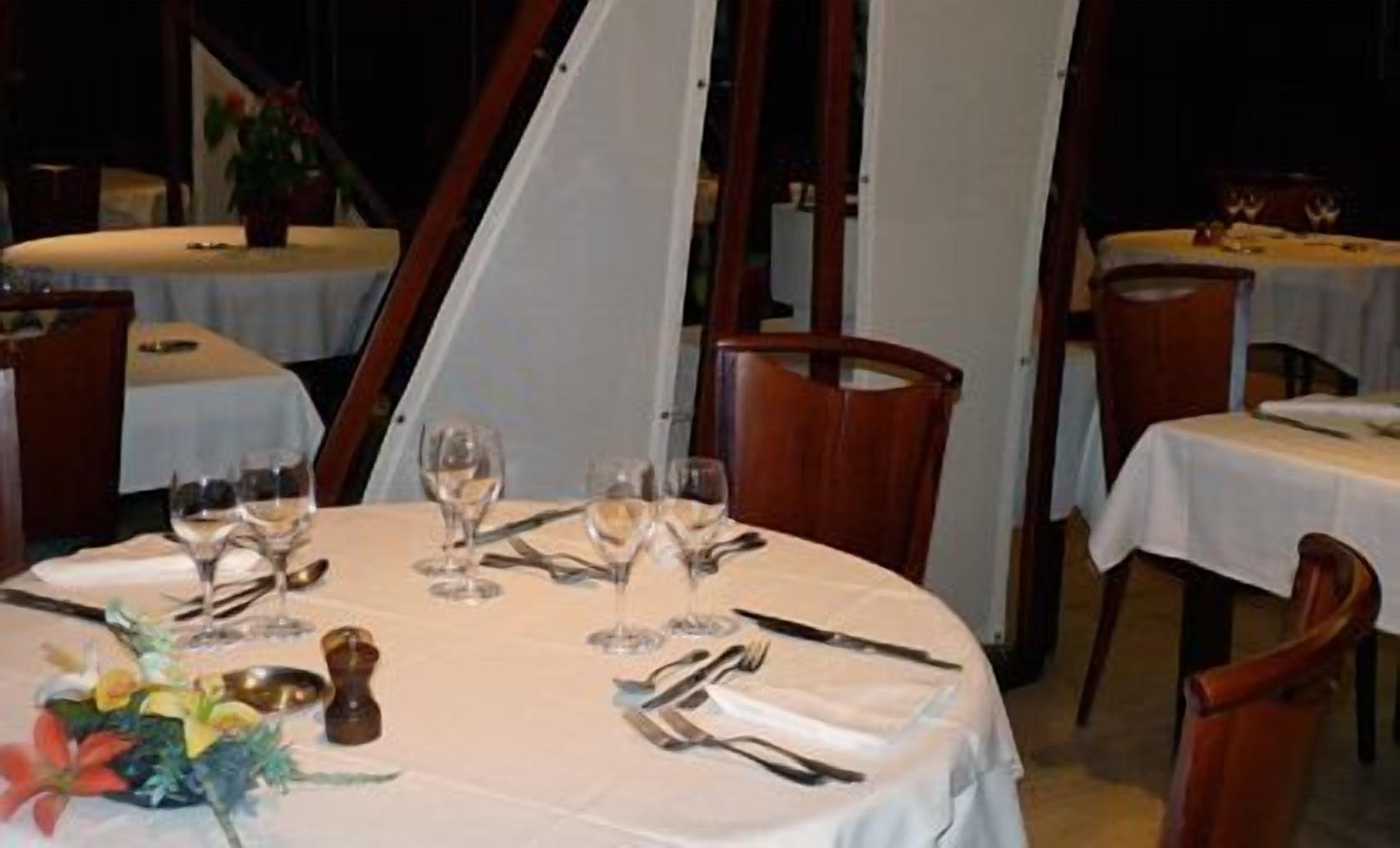 A dining area with round tables set for a meal, each table has a white tablecloth, and there are chairs around the tables.