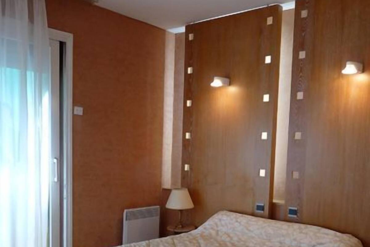 A hotel room with a large bed, a wooden accent wall, and a window with curtains.