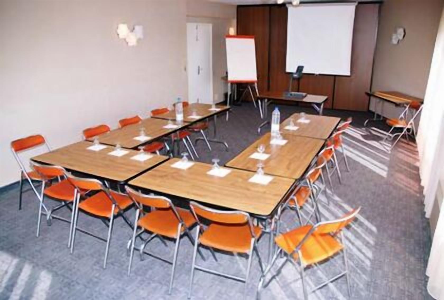 Una sala de conferencias con una gran mesa, varias sillas, una pizarra y una pantalla para proyector.