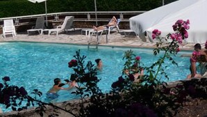 Piscina com espreguiçadeiras e guarda-sóis, cercada por vegetação.