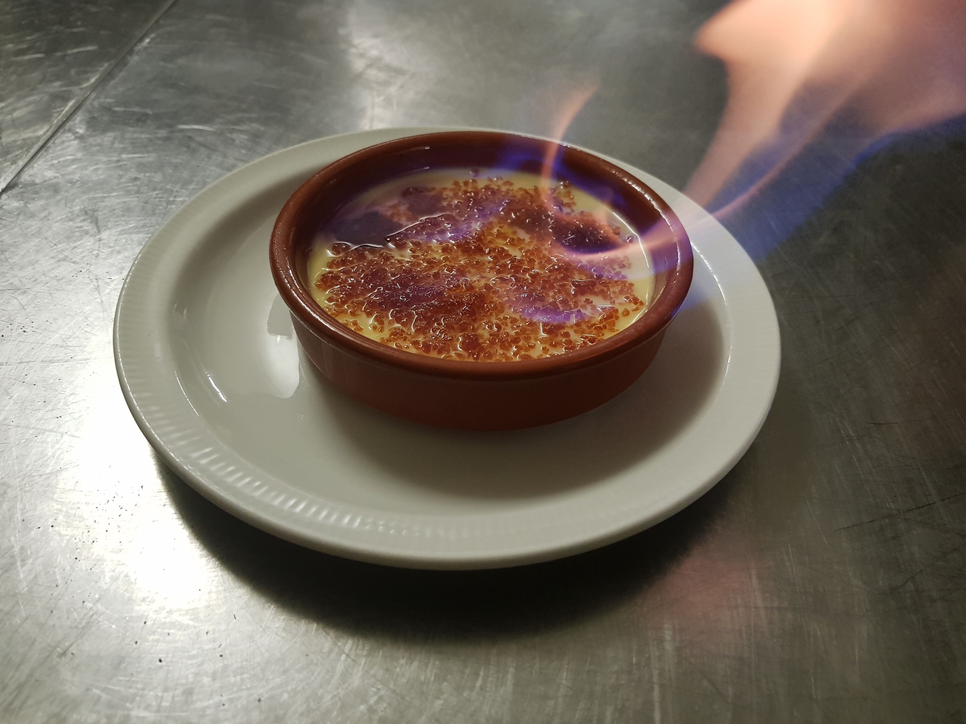 Une crème brûlée servie dans un ramequin brun sur une assiette blanche.