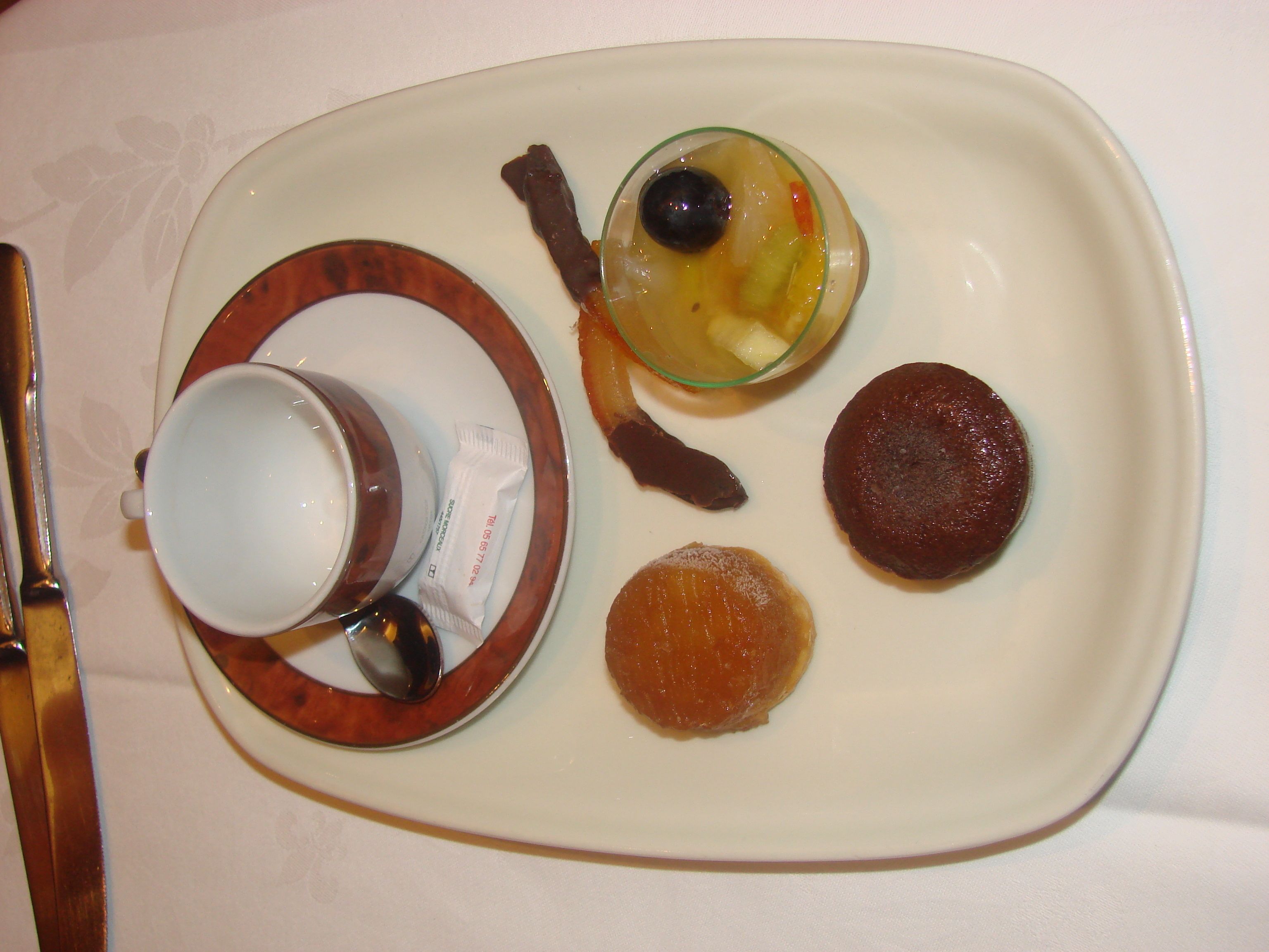A tray with a cup, a glass with fruit, and two pastries.
