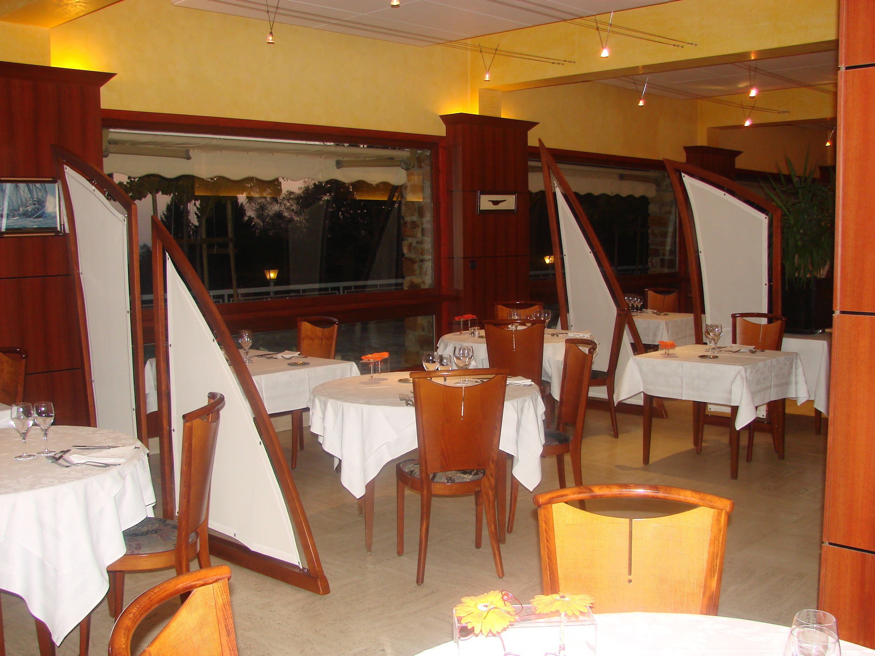 A restaurant with round tables, wooden chairs, and white tablecloths.