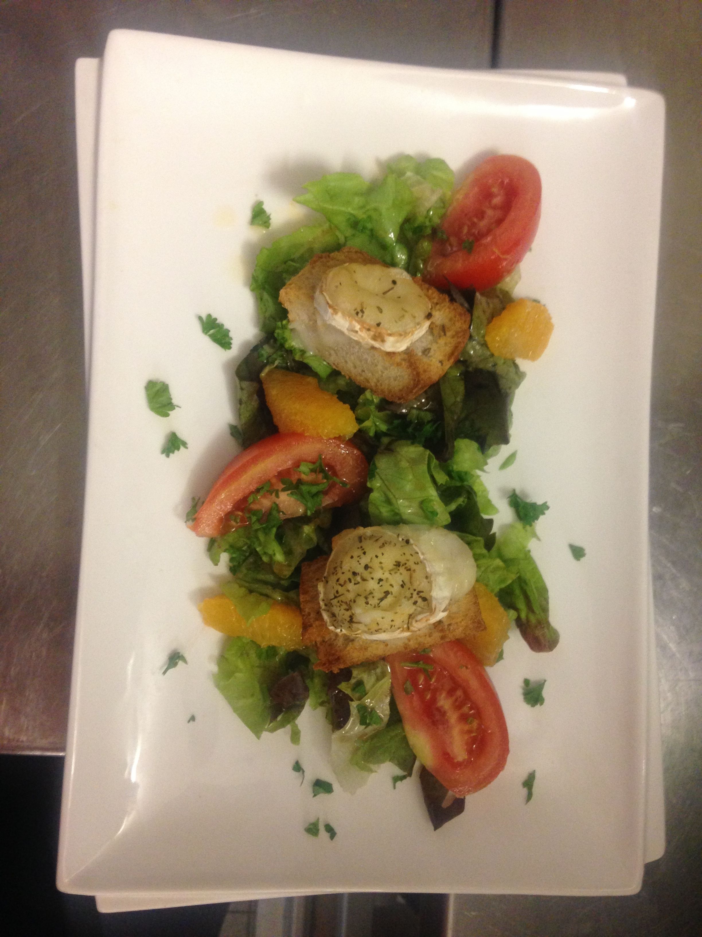 A rectangular white plate with a salad consisting of lettuce, tomatoes, and a piece of bread with a topping.