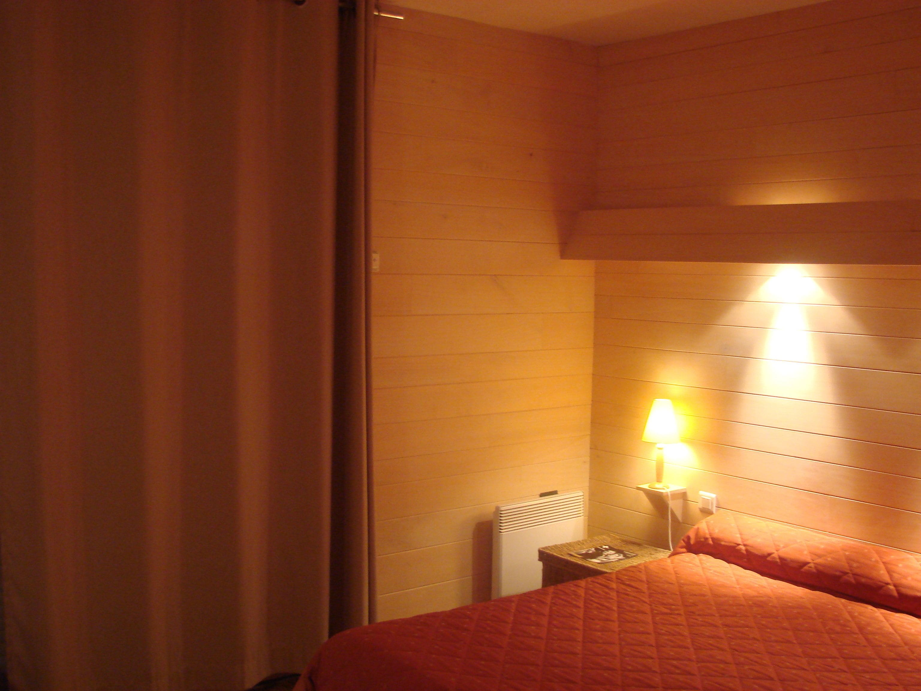 Una habitación de hotel con cama, mesita de noche, lámpara y ventana con cortinas.