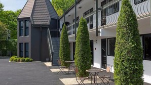 Un bâtiment moderne avec un toit gris, une structure en forme de tour et une section à toit plat dotée de balcons. On y trouve des haies soigneusement taillées et des espaces de détente en plein air.