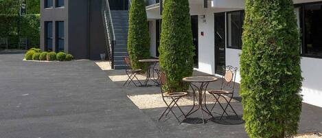A modern building with a triangular roof, a covered outdoor seating area with tables and chairs, and a parking lot.
