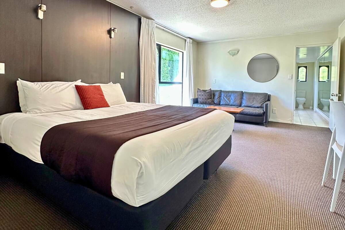 Une chambre d’hôtel avec un grand lit, un canapé, un miroir rond et une vue sur l’extérieur.