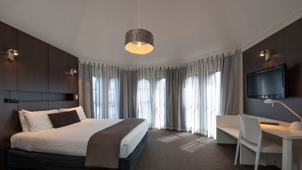 Une chambre d’hôtel moderne dotée d’un grand lit, d’un bureau, d’une télévision et d’une grande fenêtre avec des rideaux.