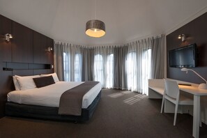A modern hotel room with a large bed, a desk, a television, and a large window with curtains. - The Towers on the Park (Christchurch)