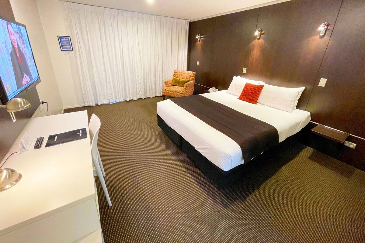 Une chambre d’hôtel équipée d’un lit, d’un bureau, d’une chaise, d’une télévision et d’une lampe fixée au mur.