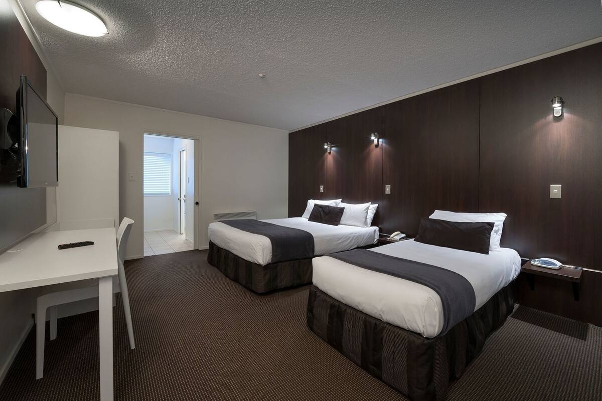 Une chambre d’hôtel avec deux lits, un bureau, une chaise, une télévision et une porte donnant sur l’extérieur.