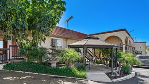 A building with a covered patio, palm trees, and a fountain. - Motel Mediteran Escondido (Escondido)