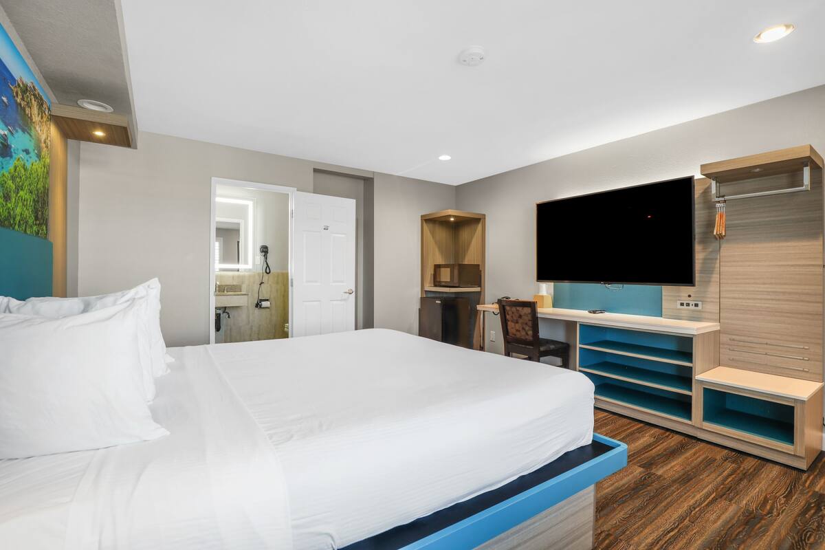 A hotel room with a bed, a TV, a desk, and a bathroom visible through an open door.