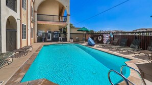 A swimming pool with lounge chairs and umbrellas, surrounded by a building with balconies and a fence. - Motel Mediteran Escondido (Escondido)