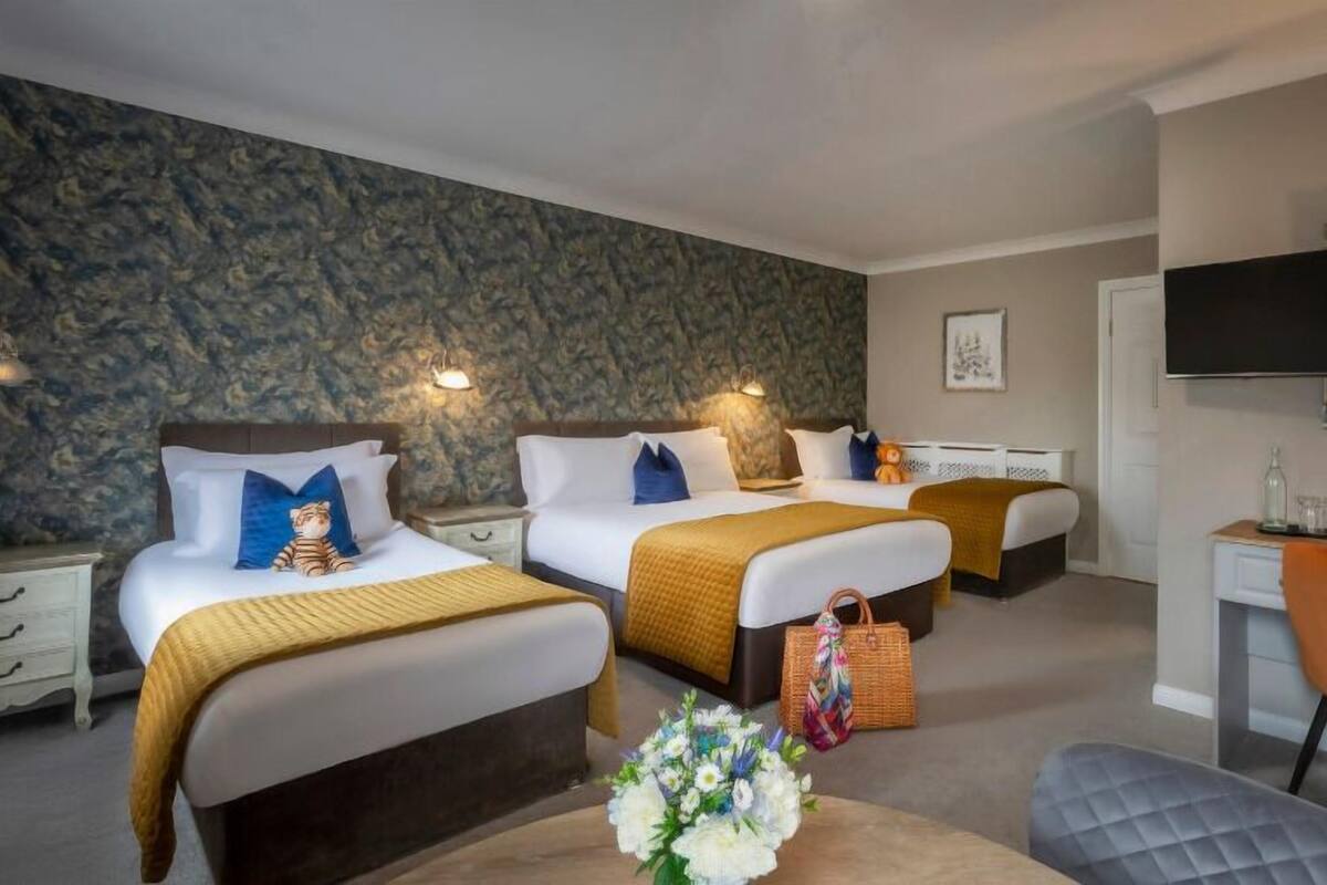 Quarto de hotel com duas camas, uma escrivaninha, uma cadeira, uma televisão e parede com padrão de pedra.