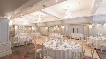 Een balzaal met ronde tafels gedekt voor een diner, kroonluchters en bloemstukken als decoratie.