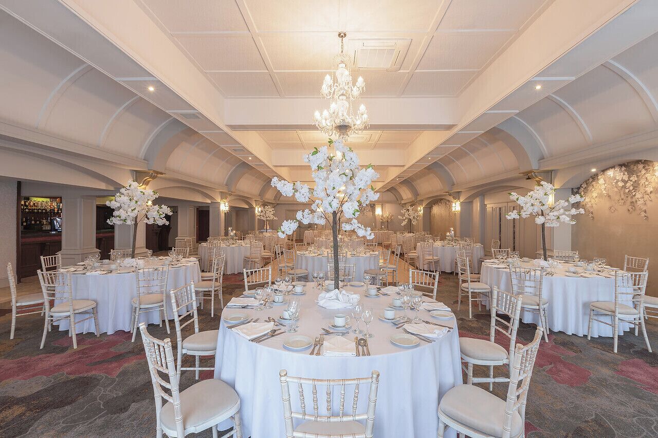 A banquet hall with round tables set for dining, white chairs, and a central chandelier.