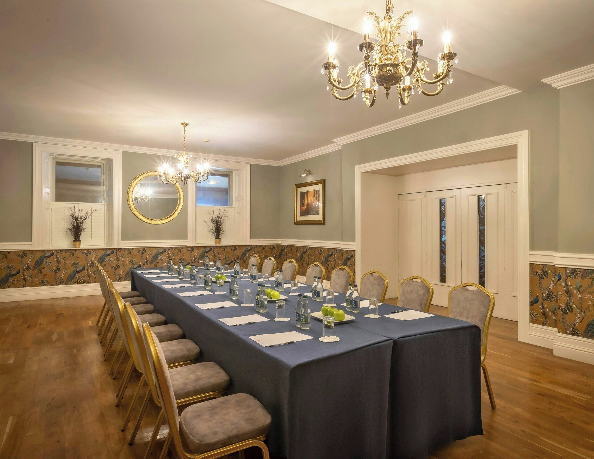 A conference room with a long table, chairs, a chandelier, and a framed picture on the wall.