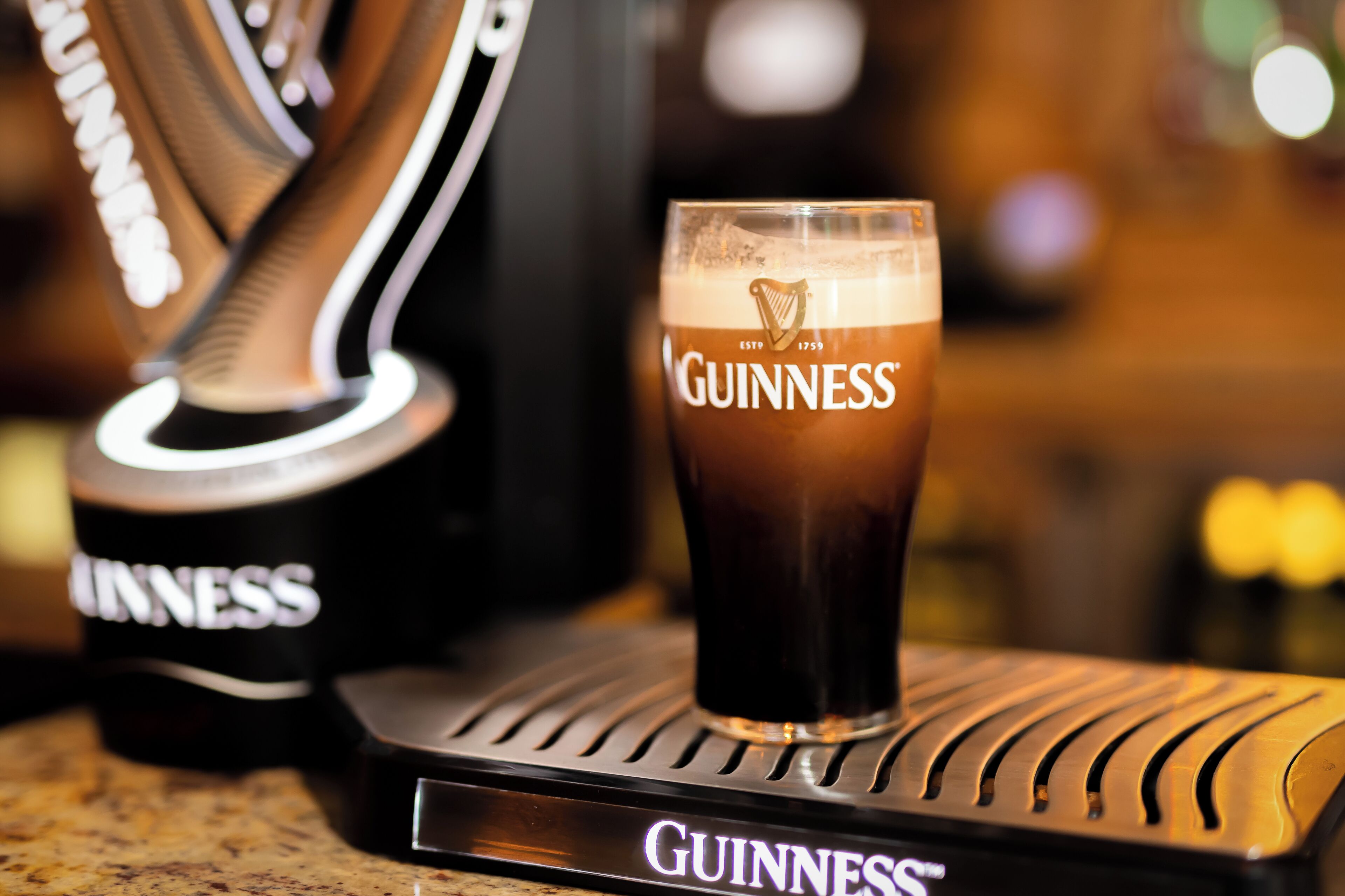 A Guinness glass on a branded coaster with a logo.