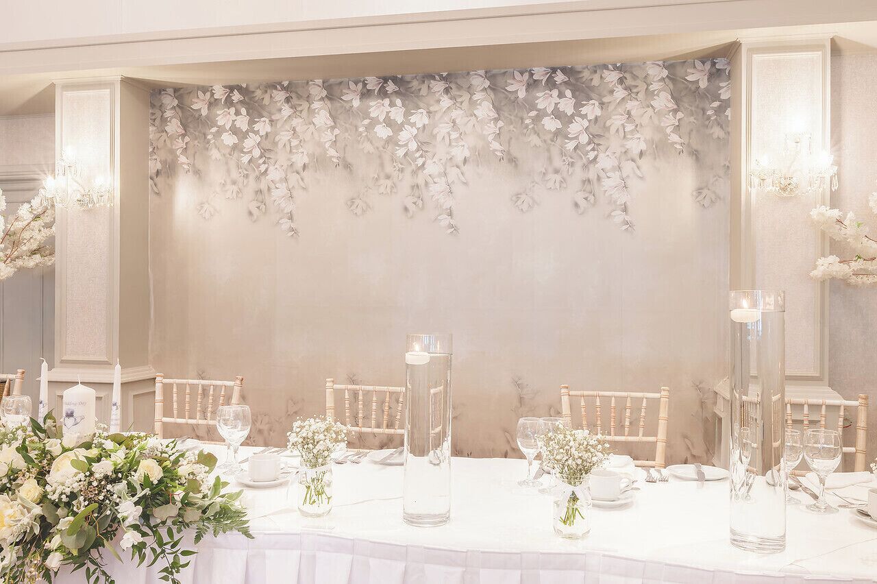 A formal dining setup with white tablecloths, tall clear vases, and floral centerpieces.