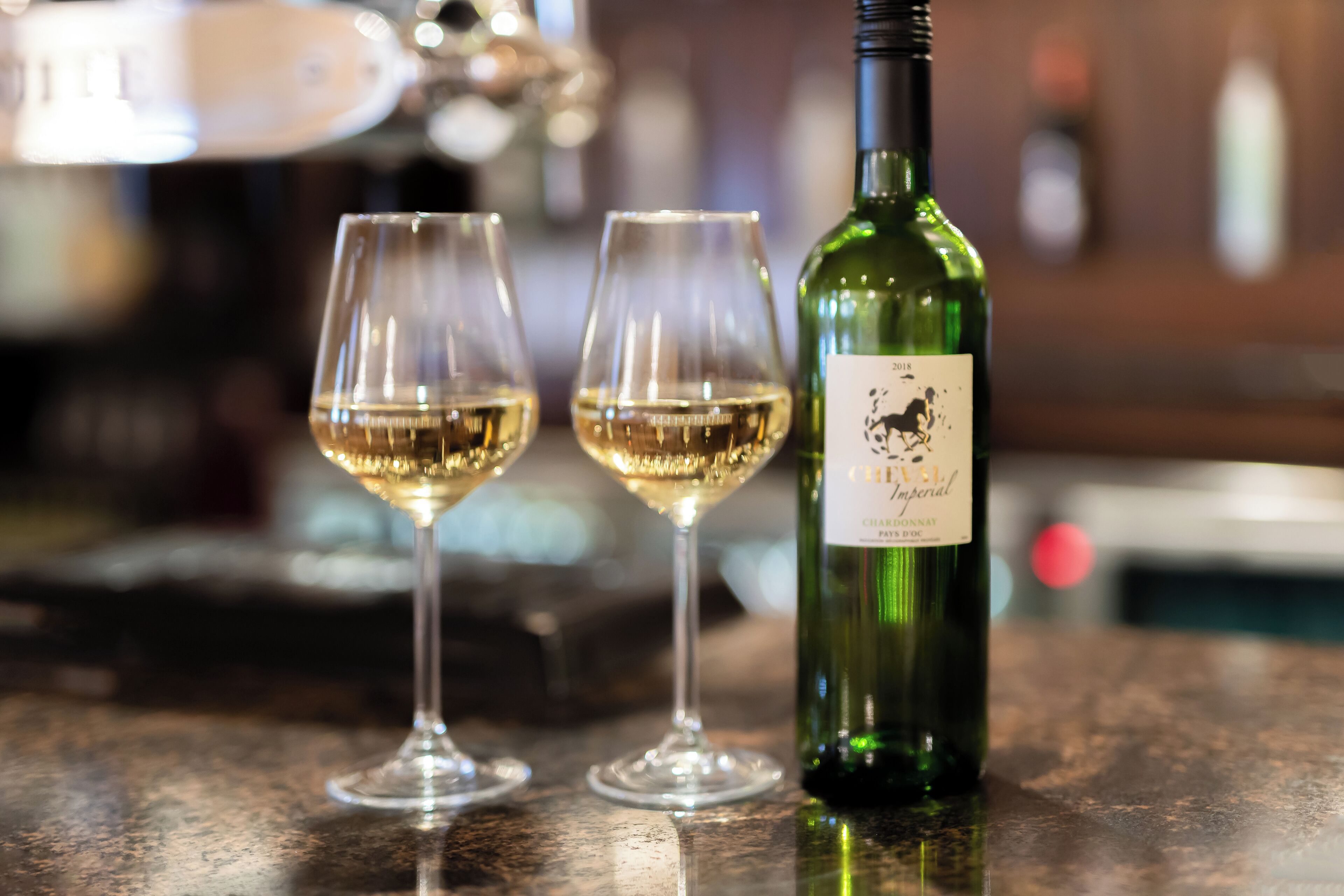 A bottle of wine and two glasses on a bar counter.