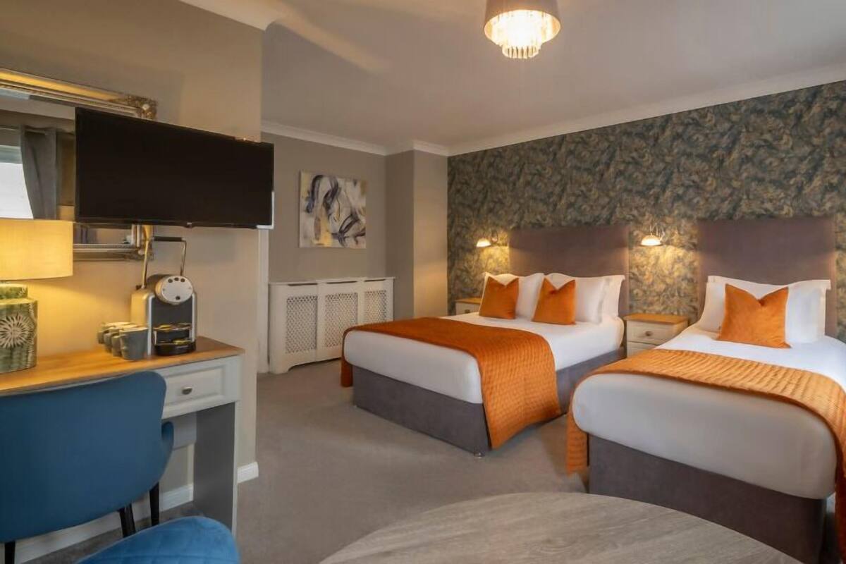 Quarto de hotel com duas camas, uma escrivaninha, uma cadeira, uma televisão e decoração na parede.