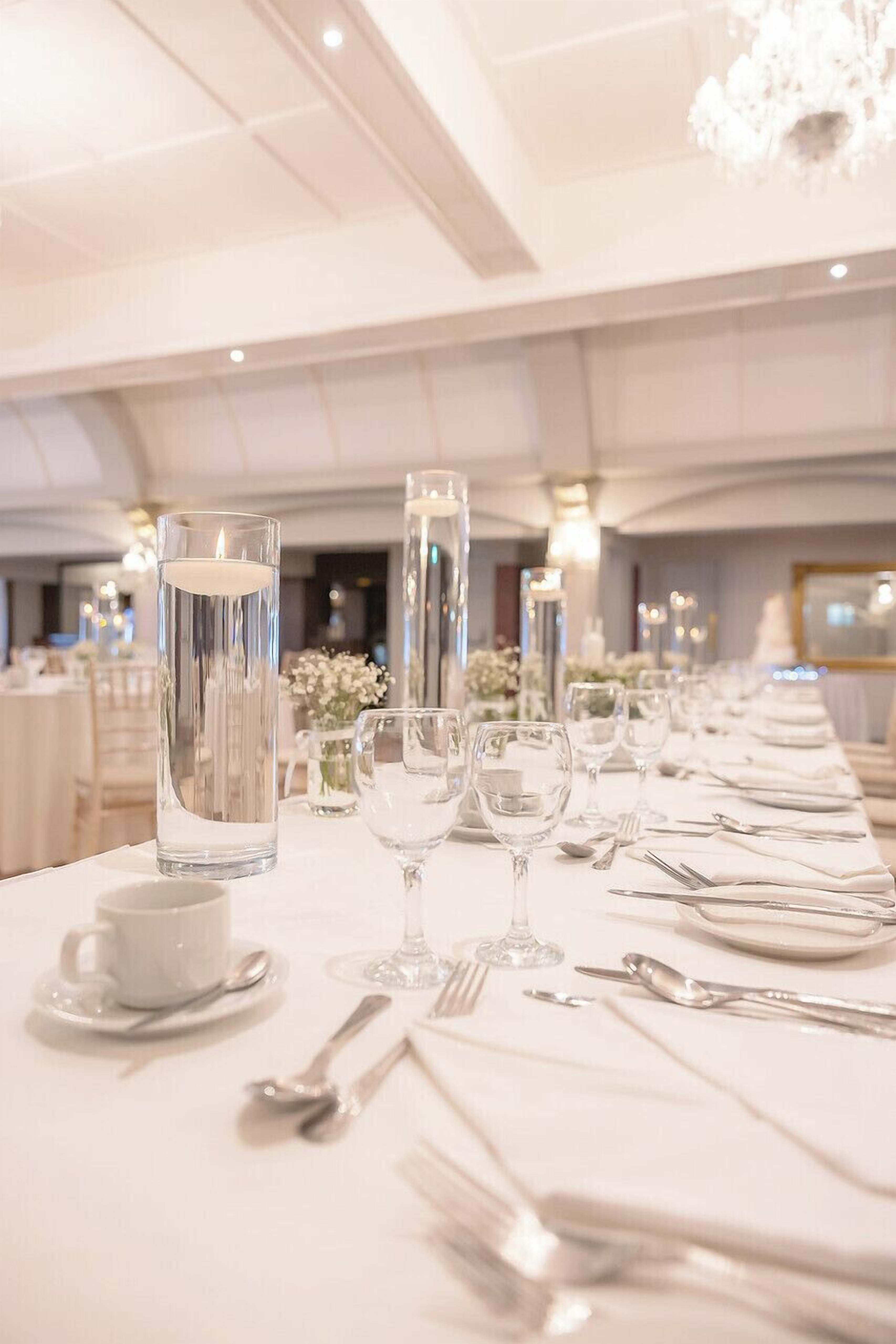 A banquet table set for a formal event, with tall glass candle holders, white tablecloths, and neatly arranged cutlery.