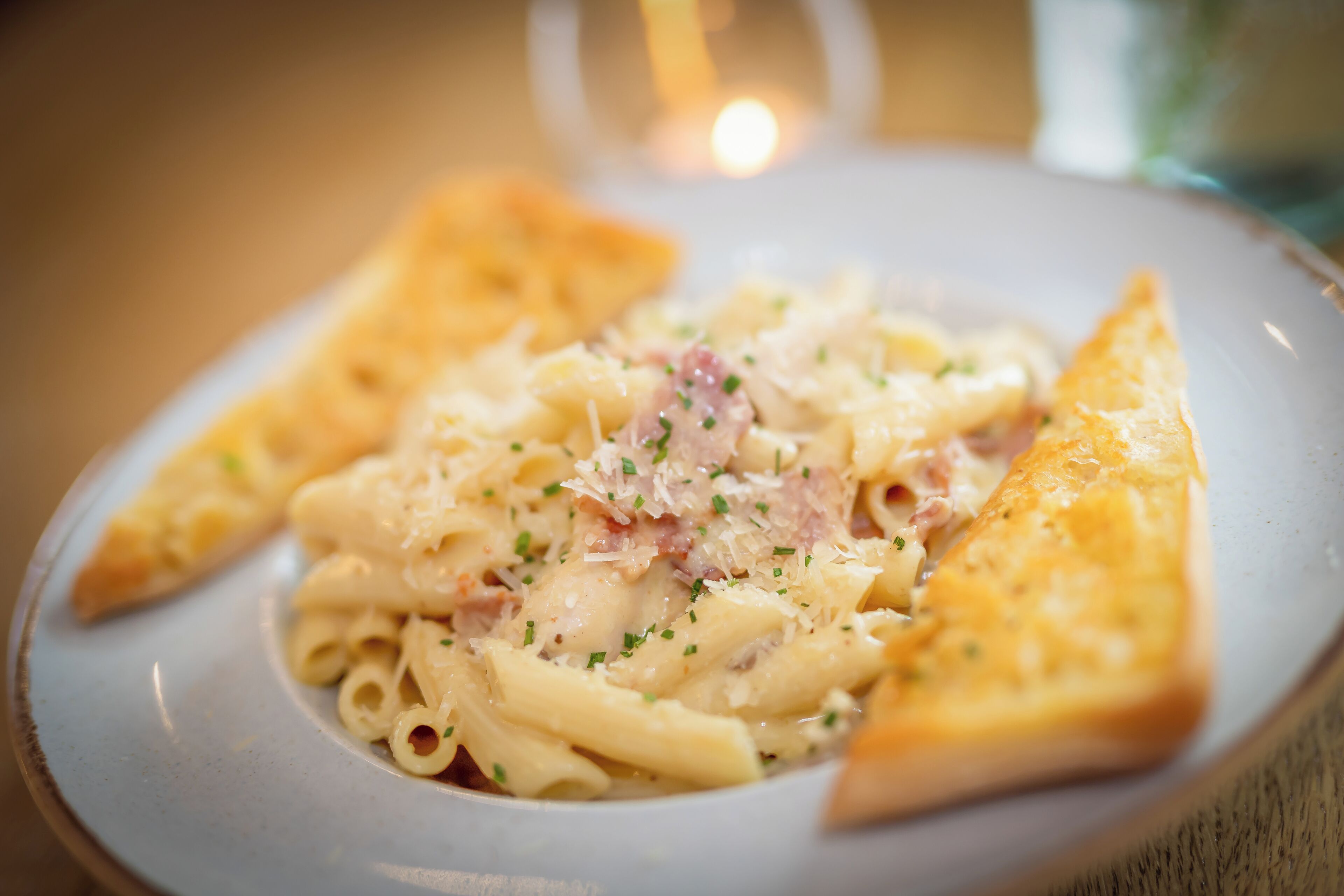 Un plato de pasta con queso y jamón, acompañado de una rebanada de pan.