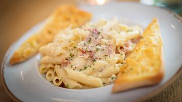 Un plato de pasta con queso y jamón, acompañado de una rebanada de pan.
