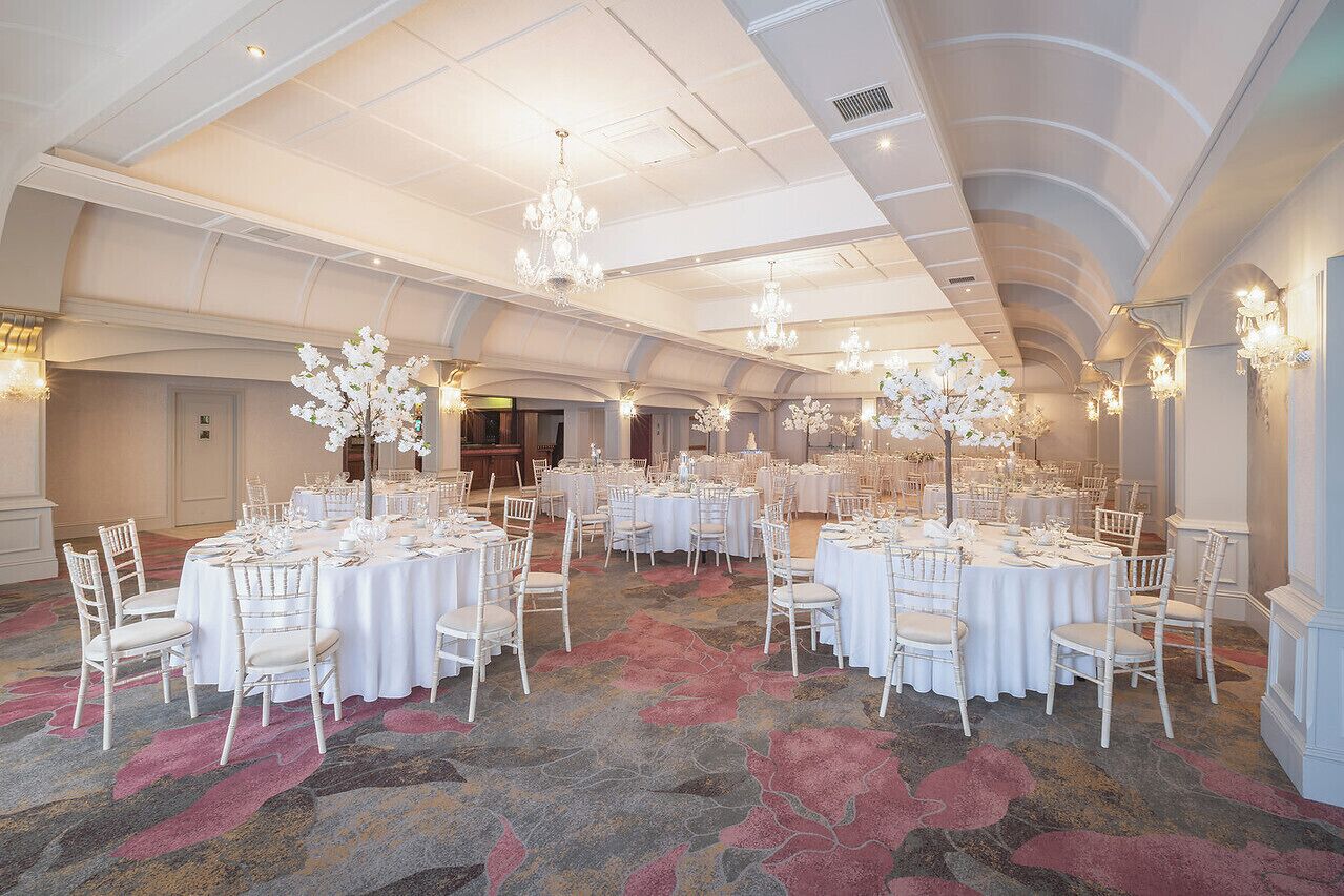 Een feestzaal met ronde tafels, witte stoelen en kroonluchters.