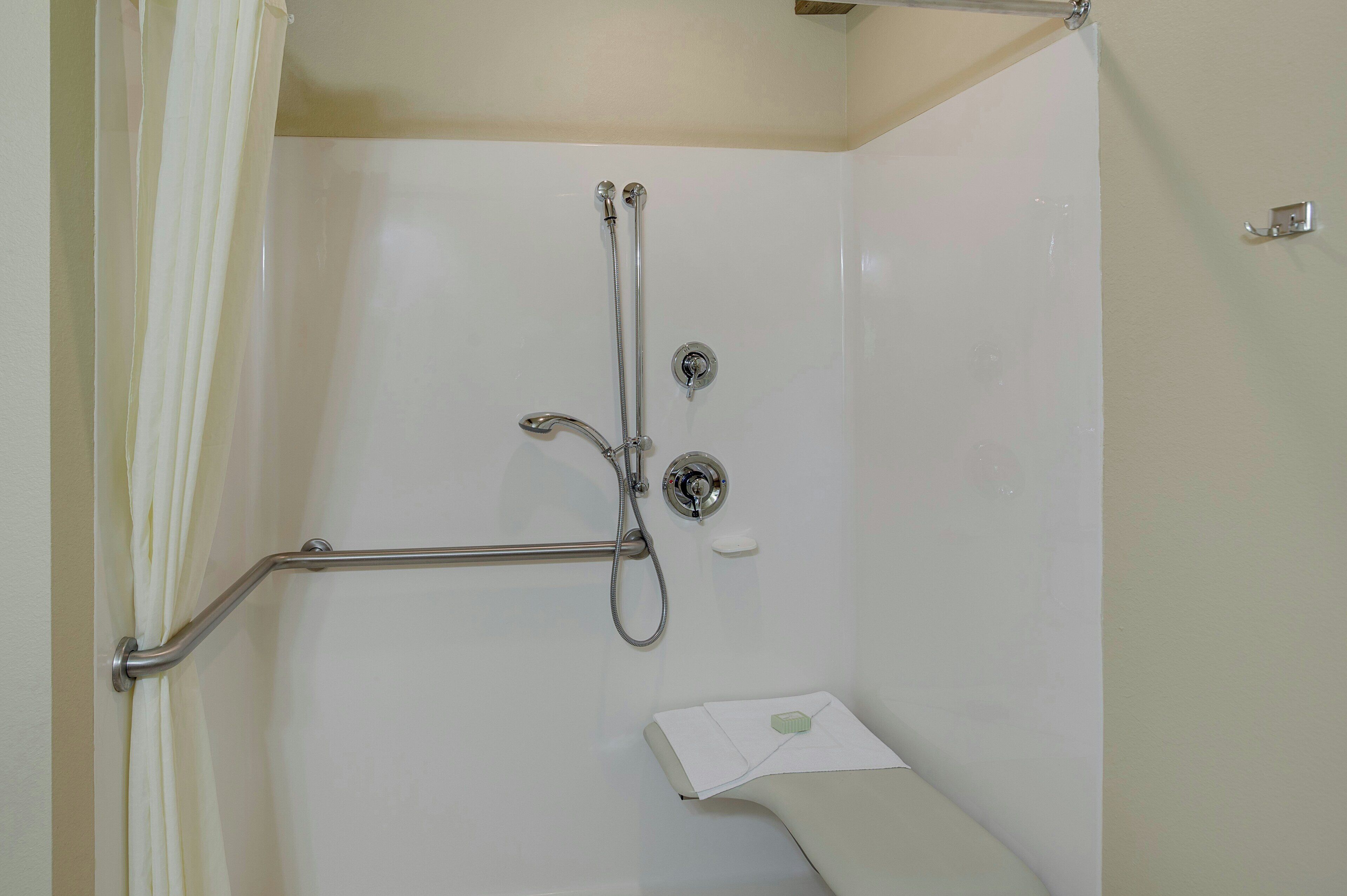 A shower with a grab bar, a handheld showerhead, and a soap dish.