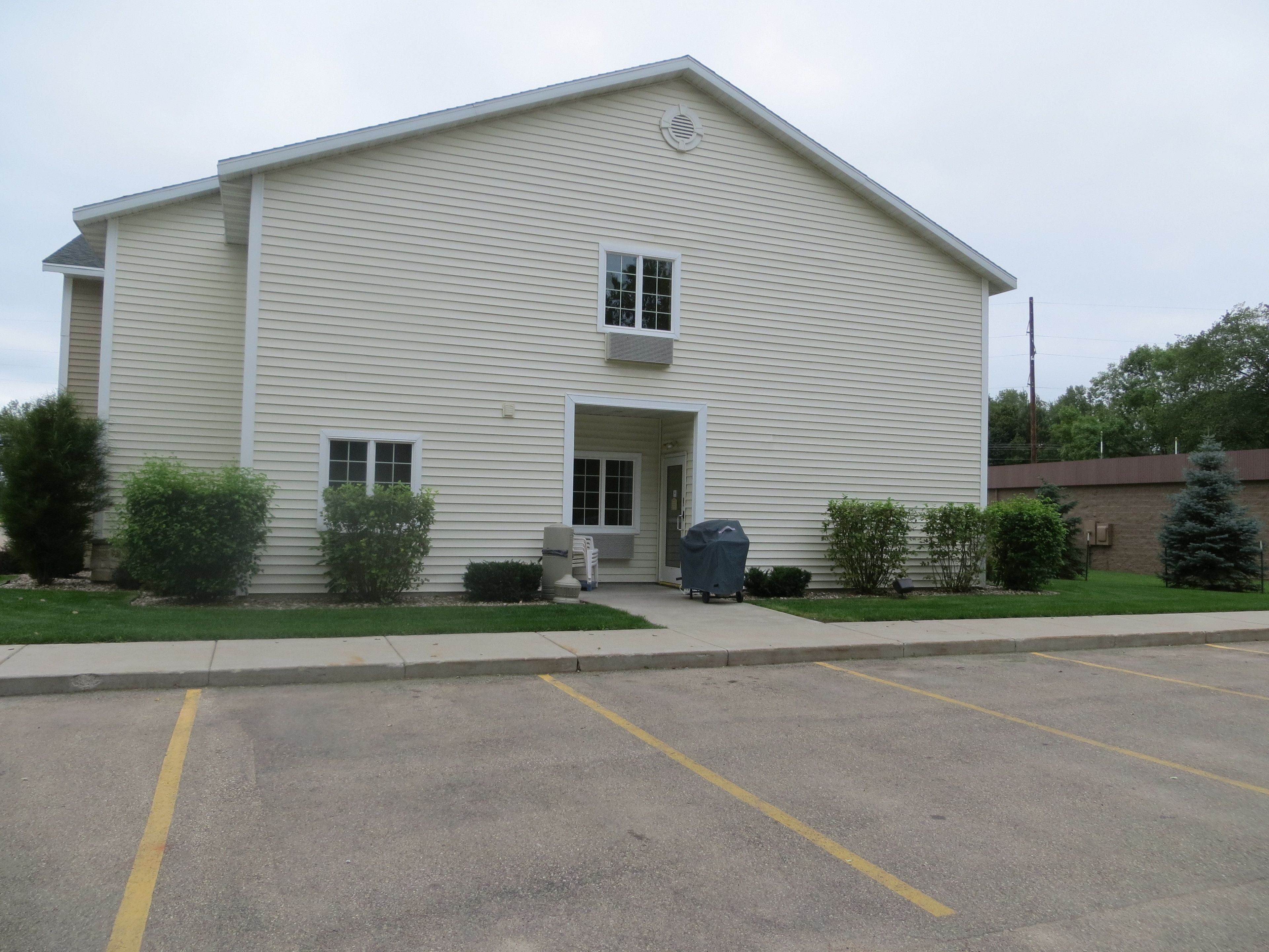 A two-story building with a flat roof, a central entrance, and a covered area with a grill.
