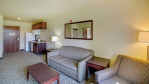 A compact hotel room with a kitchenette, a sofa, a small table, a mirror, and a lamp. - Cobblestone Inn & Suites - Brillion (Brillion)