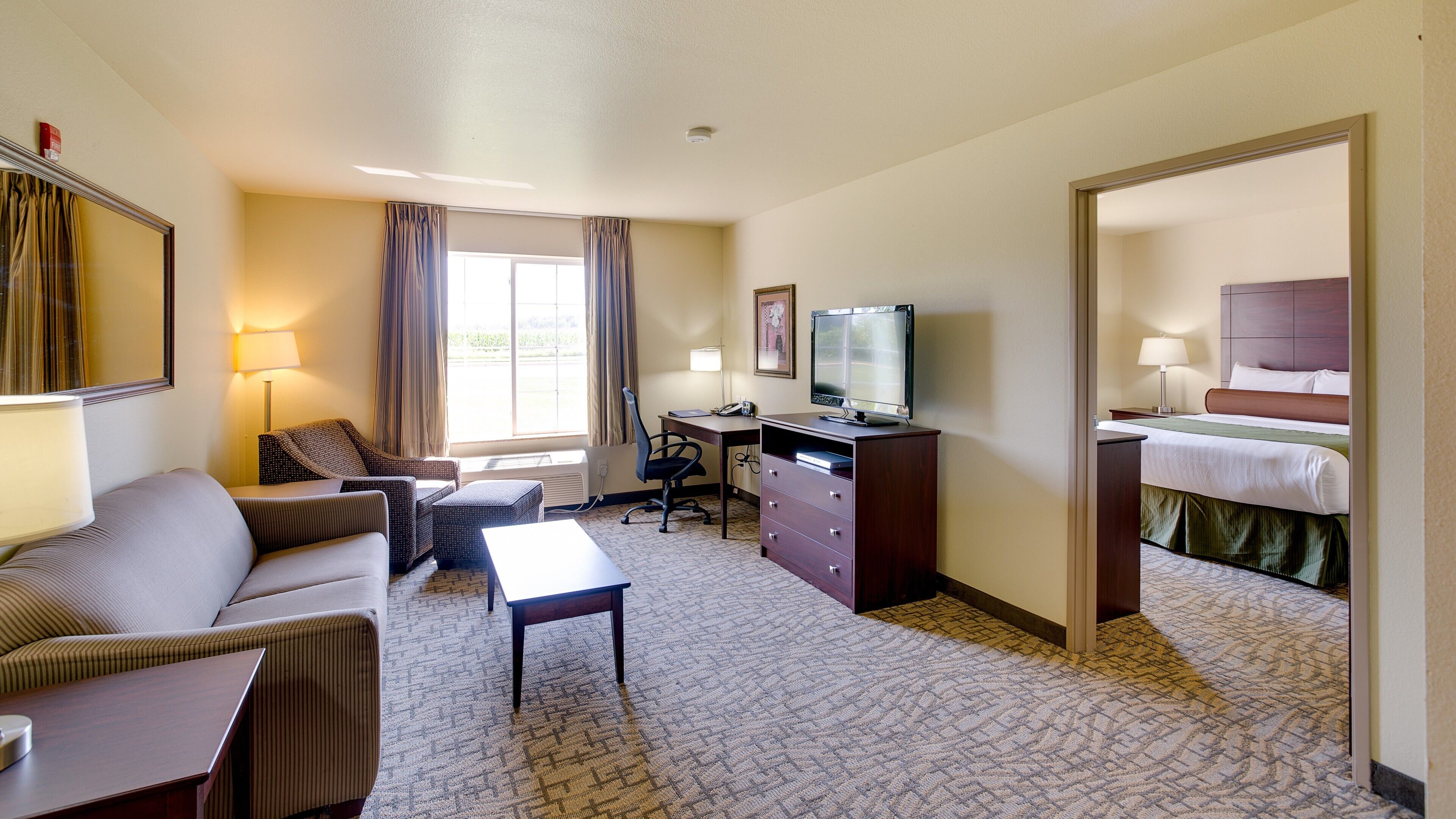 A hotel room with a sofa, a desk, a television, a dresser, and a bed.