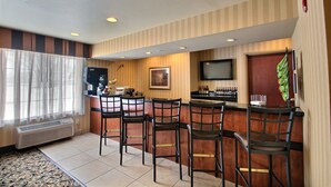 A bar area with a counter, four bar stools, a television mounted on the wall, and a door with a green curtain. - Cobblestone Inn & Suites - Brillion (Brillion)