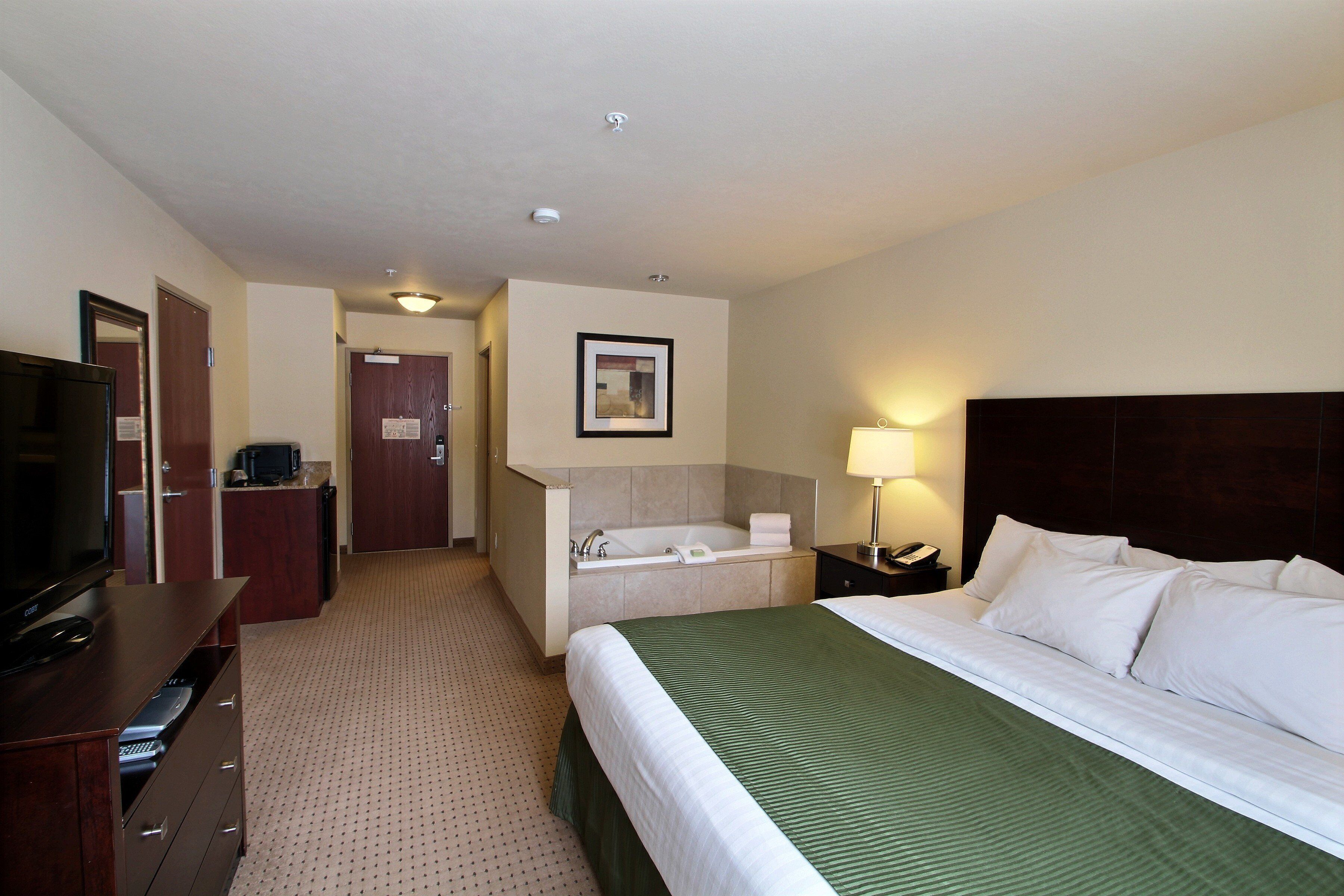 A hotel room with a bed, a TV, a desk, a lamp, a bathroom with a bathtub, and a mirror.